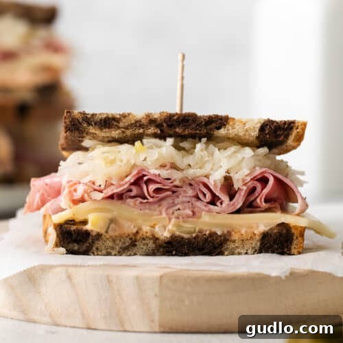 A golden-brown grilled sandwich with layers of meat and sauerkraut visible, on a wooden board.