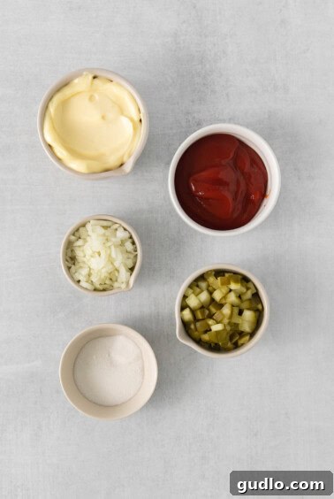 Four bowls containing separate ingredients: ketchup, mayonnaise, minced pickles, and minced onions, ready for mixing.