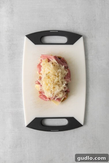 A cutting board with sliced corned beef, Swiss cheese, and bread ready for sandwich assembly.