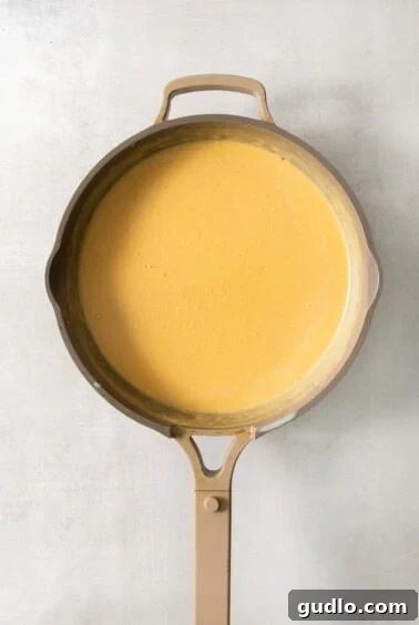 A frying pan filled with a yellow sauce, seasoned and ready for cheese.