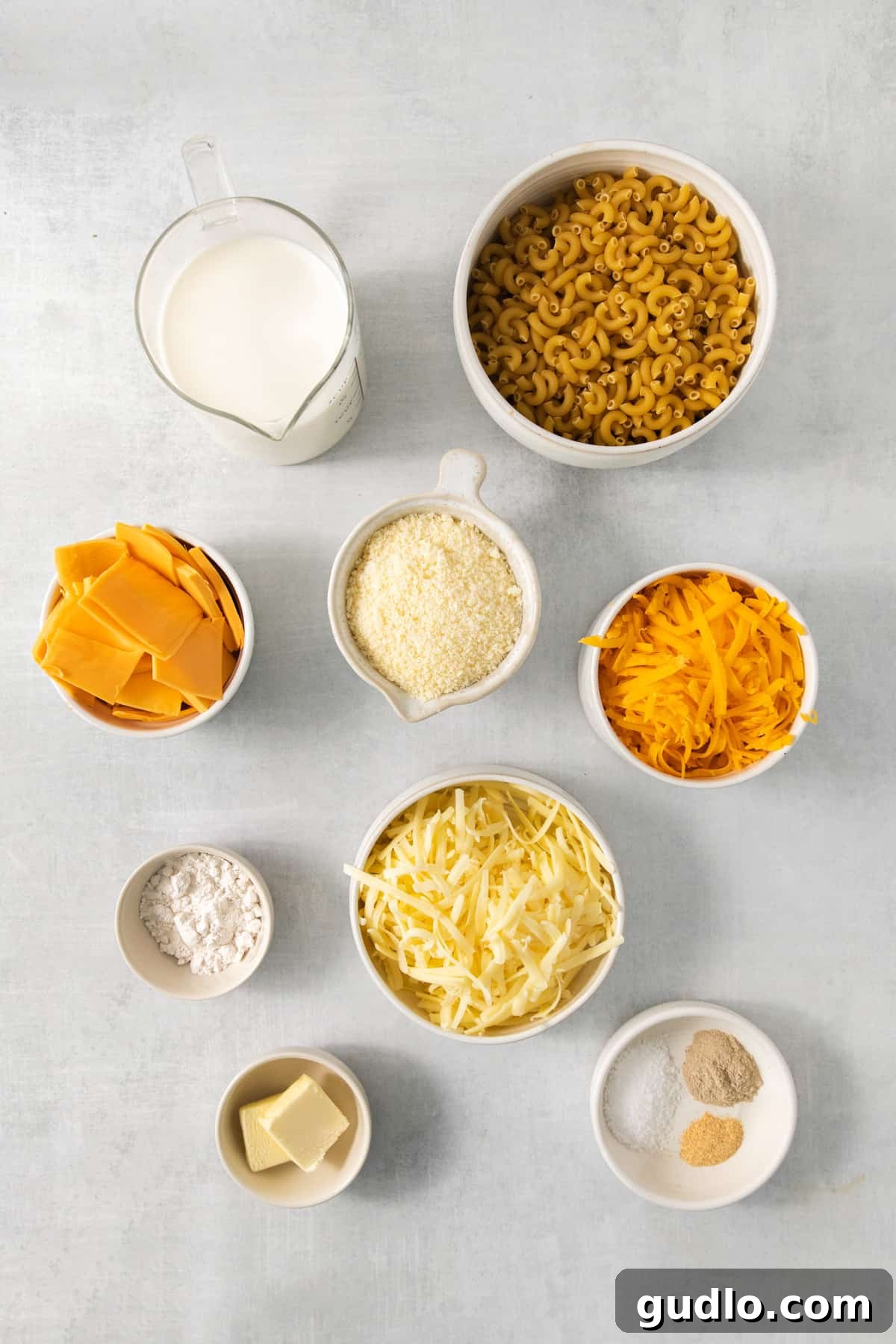 The Ultimate Chick-Fil-A Mac and Cheese Clone 3 A bowl of pasta, cheese, milk, and other ingredients laid out on a gray background, ready for cooking.