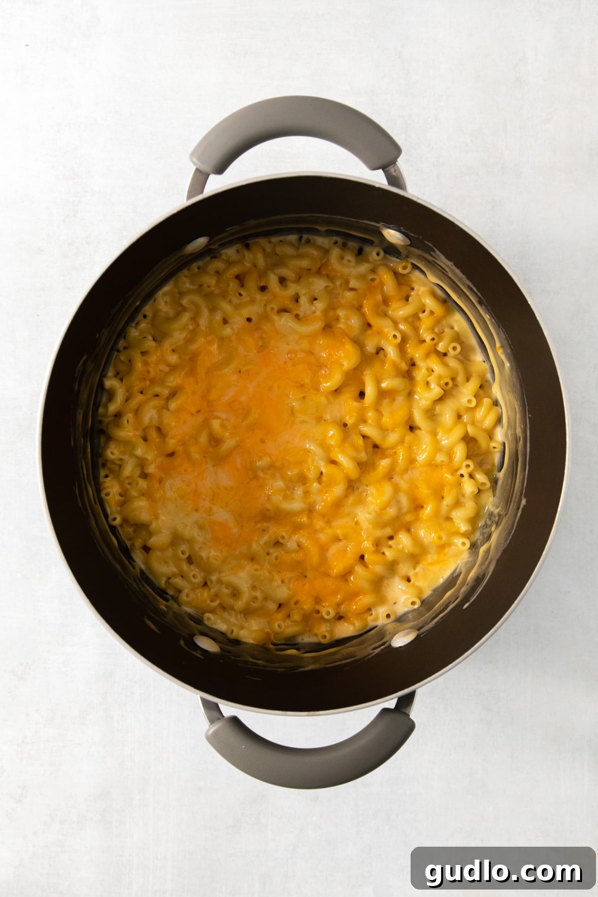 The Ultimate Chick-Fil-A Mac and Cheese Clone 5 Macaroni and cheese in a pot on a white surface, showcasing the creamy sauce clinging to the pasta.