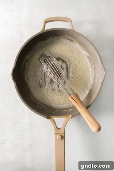 A frying pan with a whisk stirring a butter and flour roux.