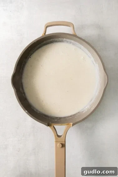 A frying pan filled with a white liquid, thickening into a béchamel sauce.