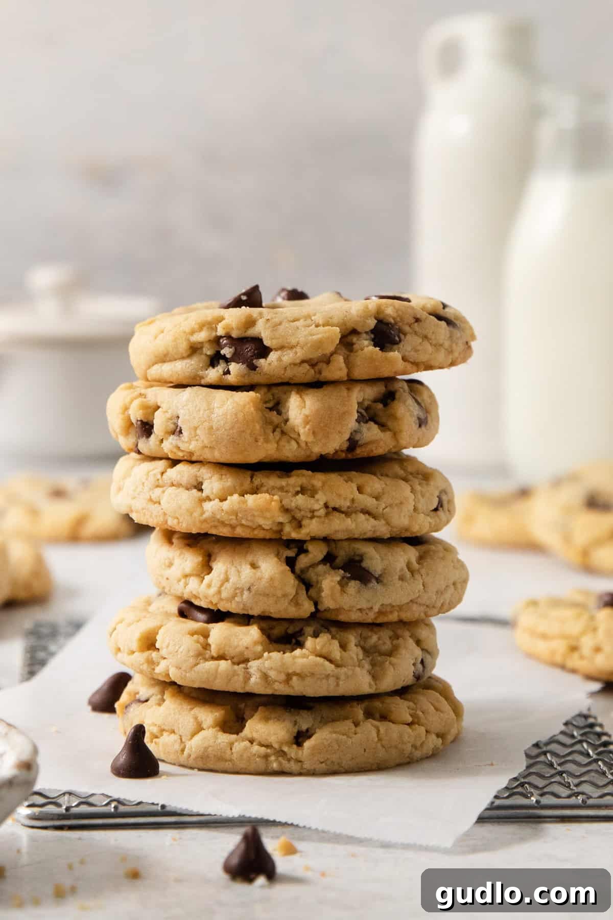 Decadent Eggless Chocolate Chip Delights 2 A stack of five egg-free chocolate chip cookies is placed on a napkin, with more cookies and bottles of milk in the blurred background.