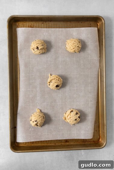 Decadent Eggless Chocolate Chip Delights 11 A baking sheet lined with parchment paper holds five scoops of egg-free chocolate chip cookie dough evenly spaced and ready for baking.