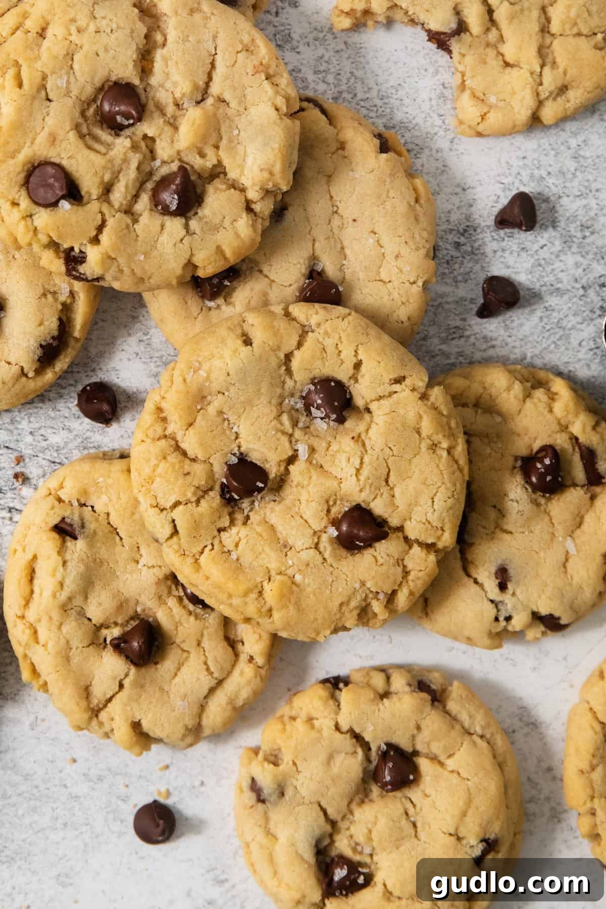 Decadent Eggless Chocolate Chip Delights 4 A close-up of several egg-free chocolate chip cookies scattered on a white surface, with some chocolate chips strewn around them.