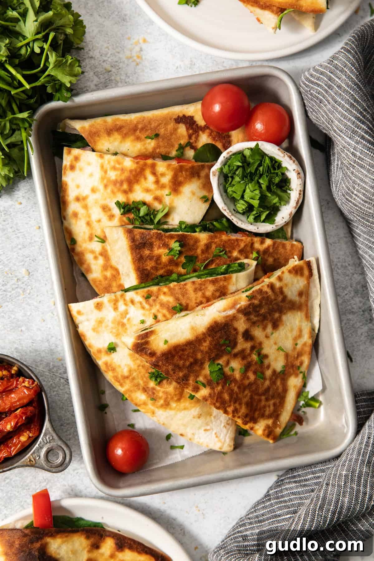 Mediterranean Sunshine Quesadilla 5 A tray of folded, golden-brown quesadillas garnished with chopped cilantro and accompanied by cherry tomatoes and a small bowl of chopped greens.