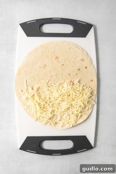 A tortilla partially filled with shredded cheese is placed on a white and black cutting board.