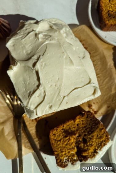 A rectangular cake with white frosting, partially sliced, sits on parchment paper with a fork beside it; a slice is served on a nearby plate.