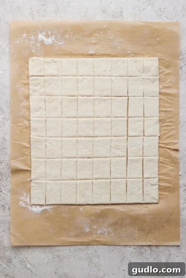 Protein Packed Pepperoni Pizza Bites 7 Square pieces of dough are evenly cut and arranged on a sheet of parchment paper atop a light, textured surface.