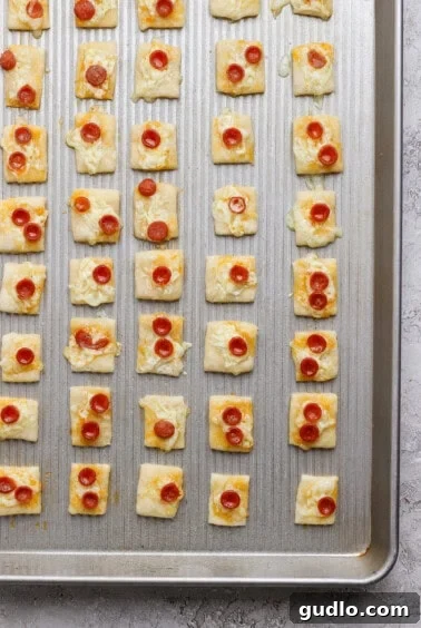 Protein Packed Pepperoni Pizza Bites 9 A baking sheet with rows of square puff pastry bites topped with melted cheese and mini pepperoni slices.