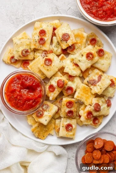 Protein Packed Pepperoni Pizza Bites 11 A plate of rectangular cheesy bread bites topped with mini pepperoni slices, served with bowls of marinara sauce and extra mini pepperoni on the side.