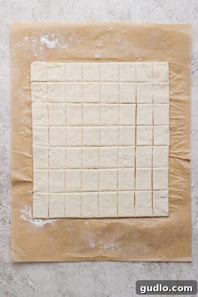 Protein Packed Pepperoni Pizza Bites 3 Square pieces of dough are evenly cut and arranged on a sheet of parchment paper atop a light, textured surface.