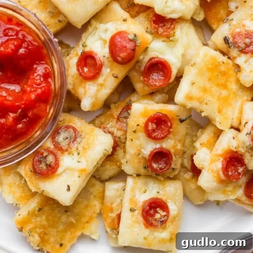 Close-up of mini cheese and pepperoni pizza bites on a plate with a small bowl of marinara dipping sauce.