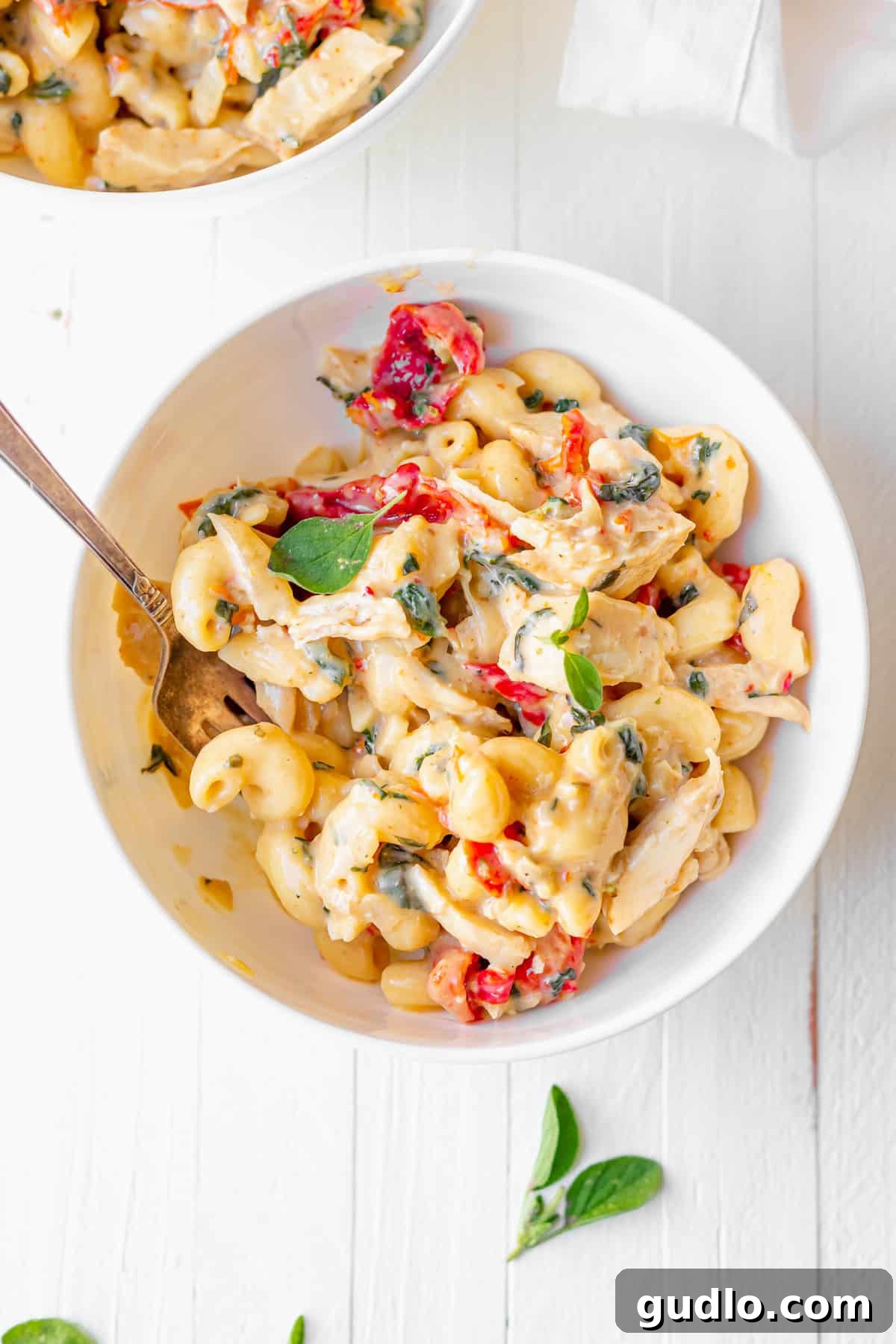 This Tuscan Chicken Mac and Cheese offers fancy comfort food at its finest! Its rich, delicious flavors and unbeatable cheesy goodness will undoubtedly make it a new family favorite in your home, too. A generous bowl of creamy Tuscan chicken mac and cheese, garnished with fresh basil, ready to be enjoyed.