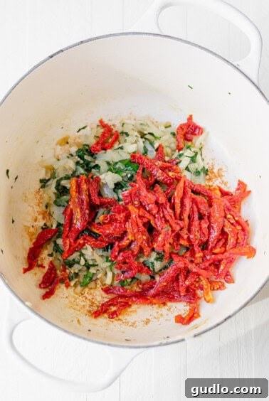 A colorful medley of onions, garlic, spinach, and sun-dried tomatoes sautéing together for the Tuscan Chicken Mac and Cheese, filling the kitchen with incredible aromas.