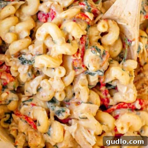 A beautifully presented Tuscan chicken mac and cheese dish, served with a wooden spoon, inviting you to taste its gourmet flavors.