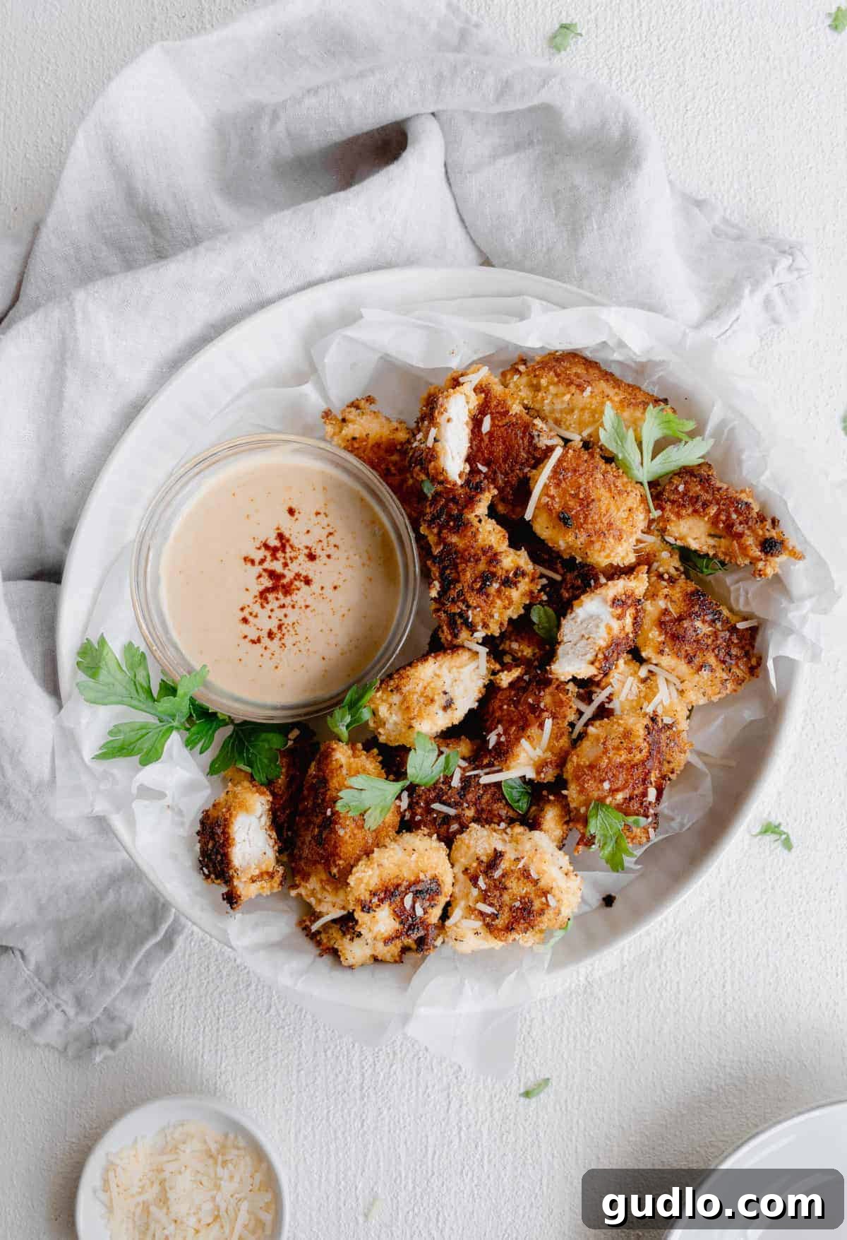 Golden-brown Parmesan Chicken Nuggets ready to be enjoyed. Crispy Parmesan chicken nuggets served on a plate with dipping sauce, garnished with fresh parsley.