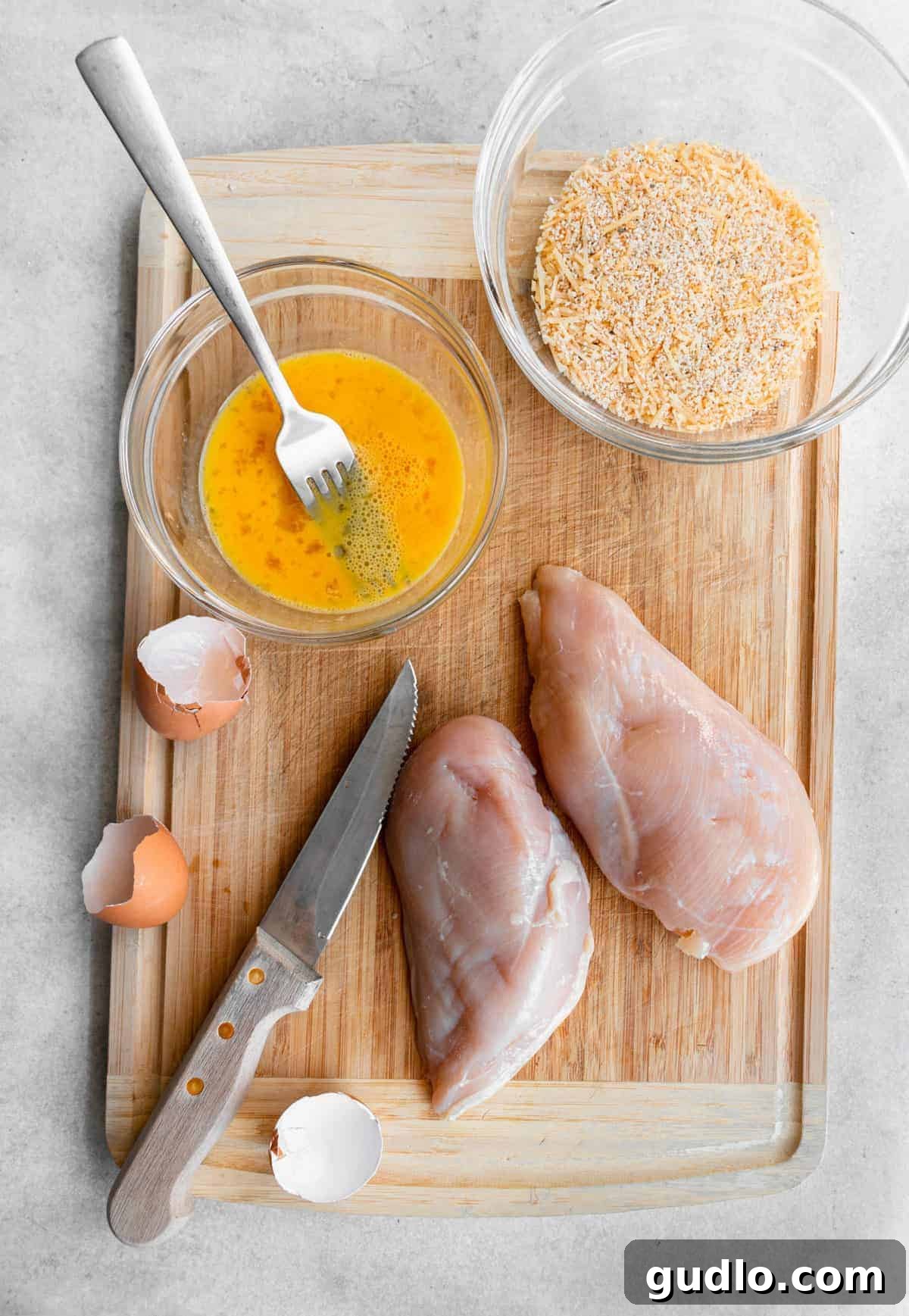 Fresh ingredients ready for homemade chicken nugget preparation. A selection of raw ingredients for Parmesan chicken nuggets, including cubed chicken, eggs, breadcrumbs, and spices, laid out on a wooden cutting board.