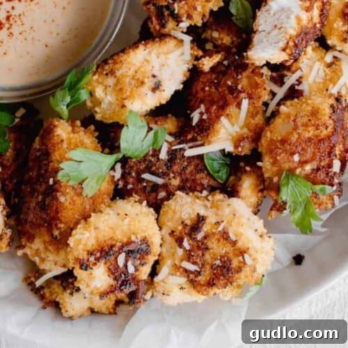 Fried chicken nuggets with dipping sauce served on a plate, garnished with fresh herbs.