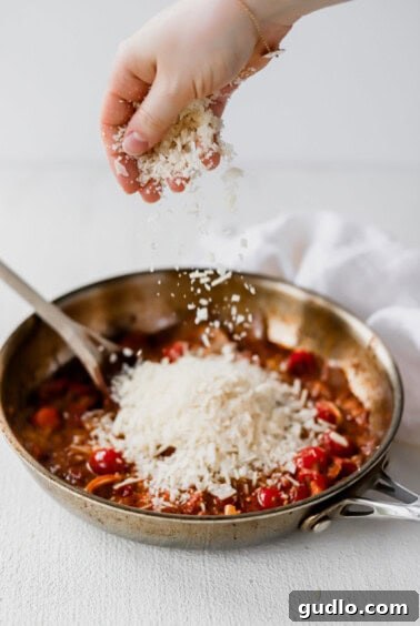 A person sprinkling parmesan on sun dried tomato pasta.