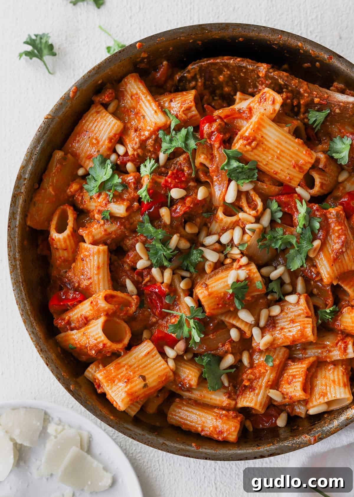 A bowl of sun dried tomato pasta generously topped with fresh parsley and crunchy pine nuts.