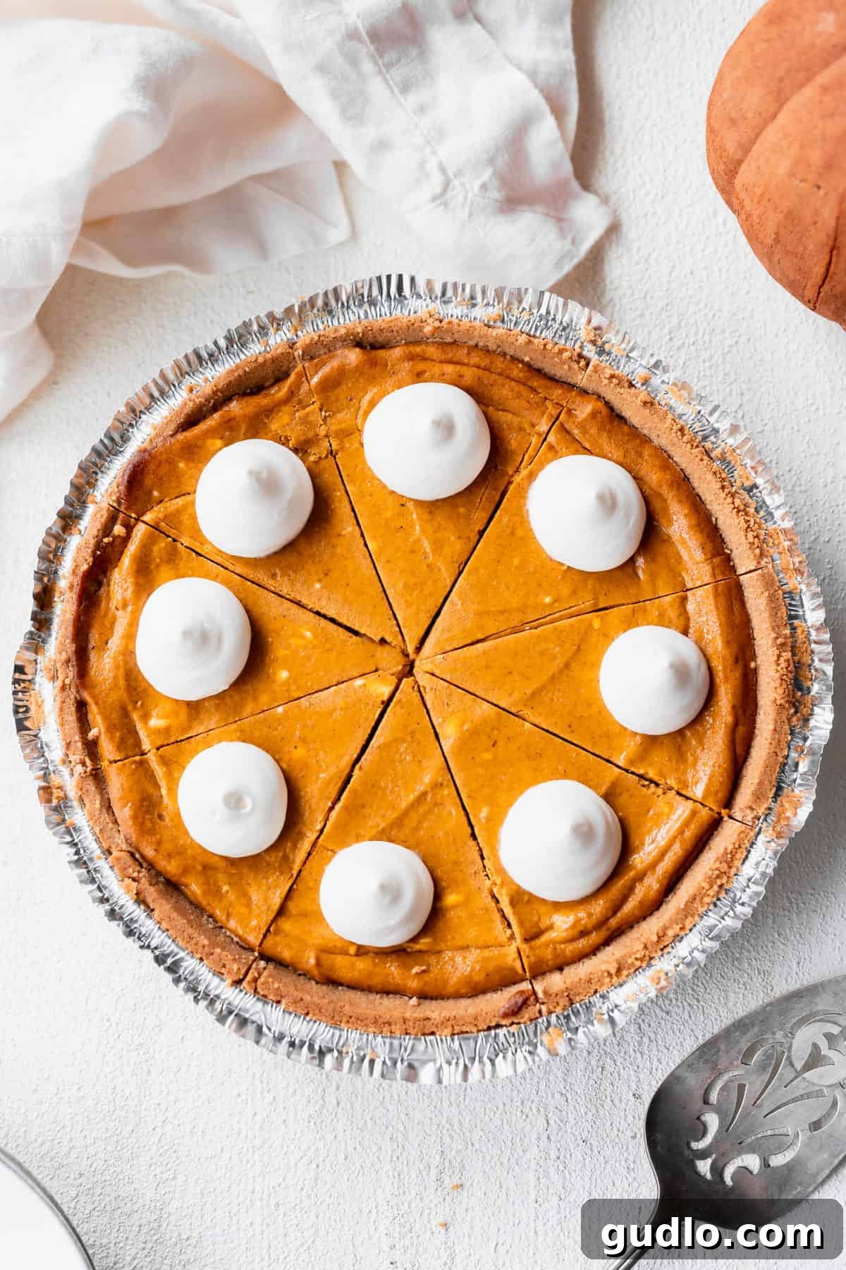 Effortless Pumpkin Cheesecake 2 Decadent pumpkin cheesecake, perfectly baked in a pie tin, adorned with generous dollops of fluffy whipped cream on top, ready to be served.