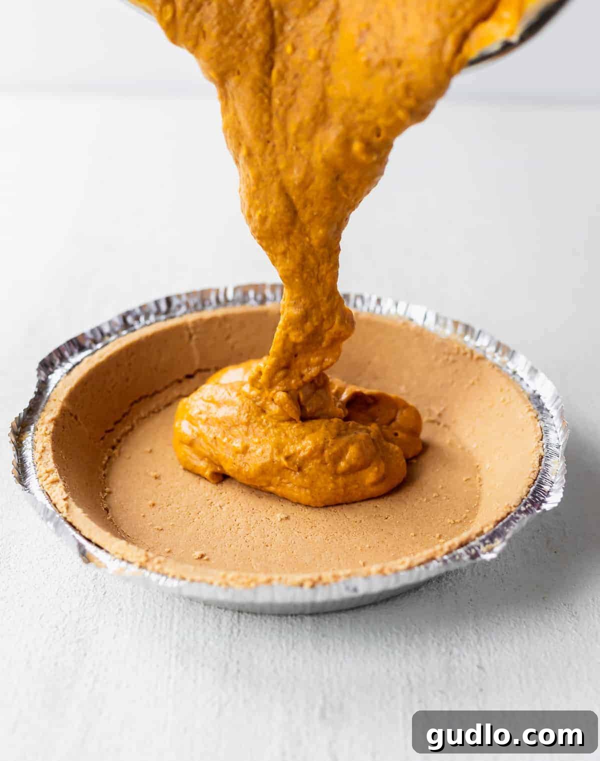 Effortless Pumpkin Cheesecake 4 Smooth and creamy pumpkin cheesecake filling being carefully poured into a pre-made graham cracker pie crust, ready for baking to create a delicious dessert.