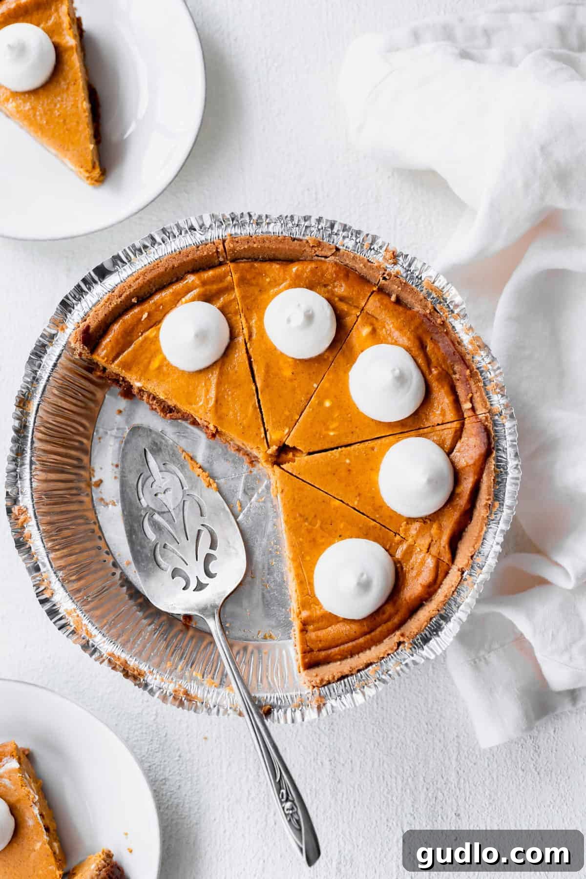 Effortless Pumpkin Cheesecake 5 A perfectly baked pumpkin cheesecake, still in its pie tin, with several slices already cut, revealing its creamy texture and golden-brown graham cracker crust.