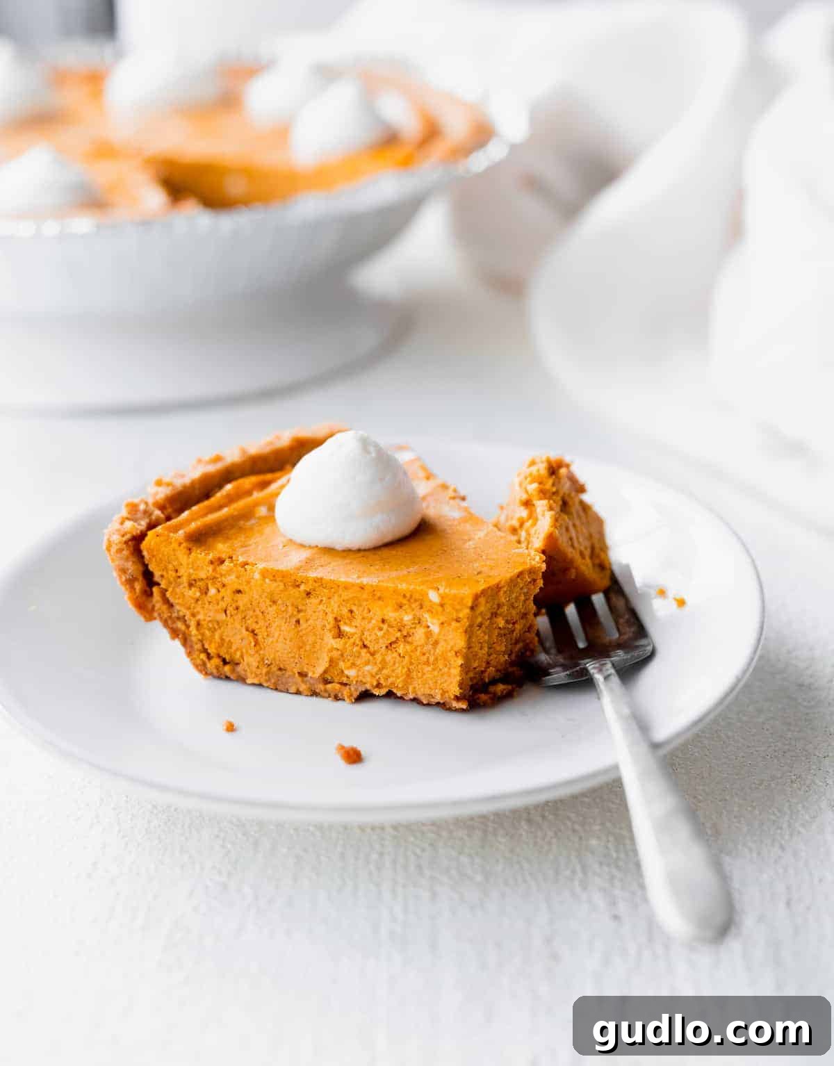Effortless Pumpkin Cheesecake 6 A perfectly portioned slice of creamy pumpkin cheesecake resting on a pristine white dessert plate, beautifully adorned with whipped cream and a delicate sprinkle of warming spice.