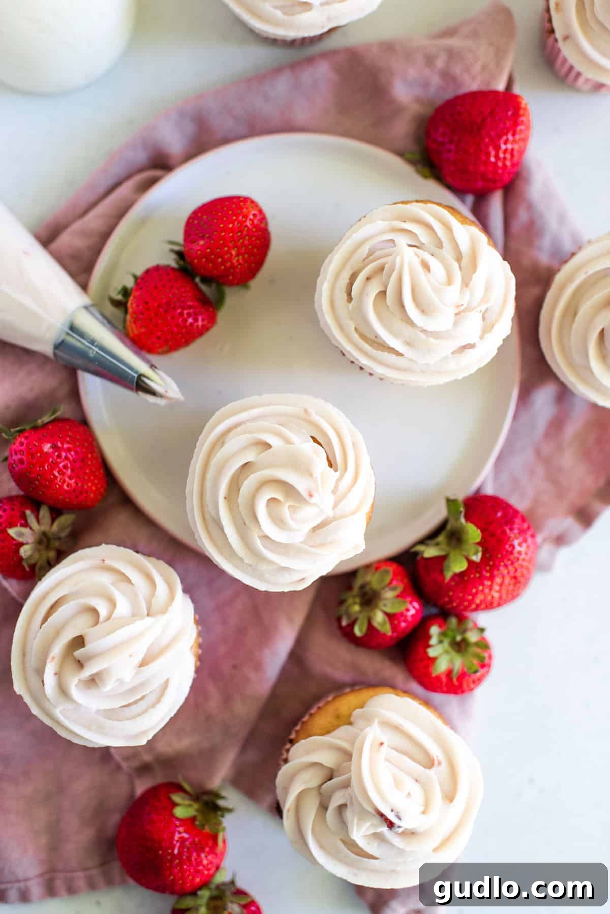 Strawberry Cream Cheese Frosting piped onto cupcakes. Strawberry cream cheese frosting elegantly piped onto delicious cupcakes, garnished with fresh strawberry slices.