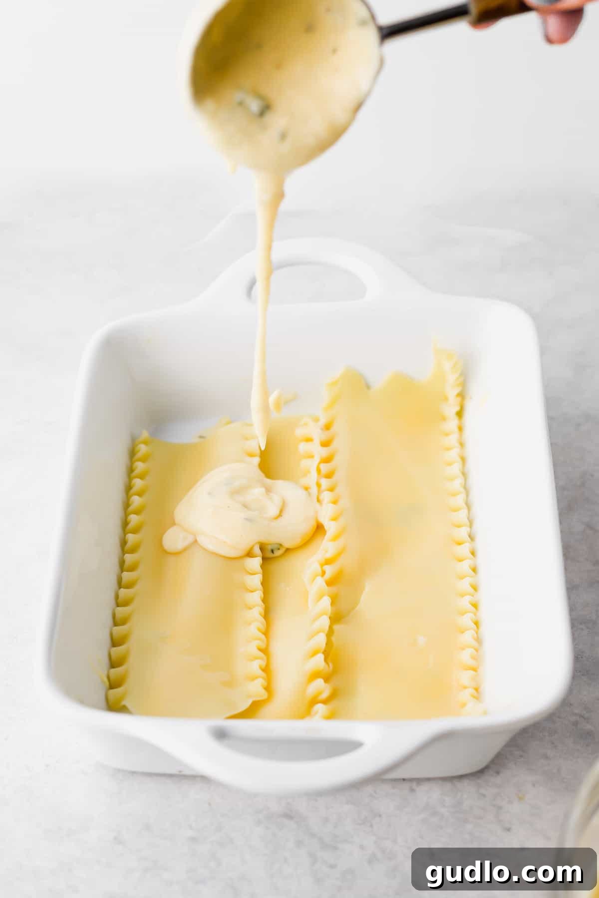 Decadent Chicken Alfredo Lasagna 6 Rich, creamy cheese sauce being generously poured over delicate pasta noodles, promising a decadent meal.