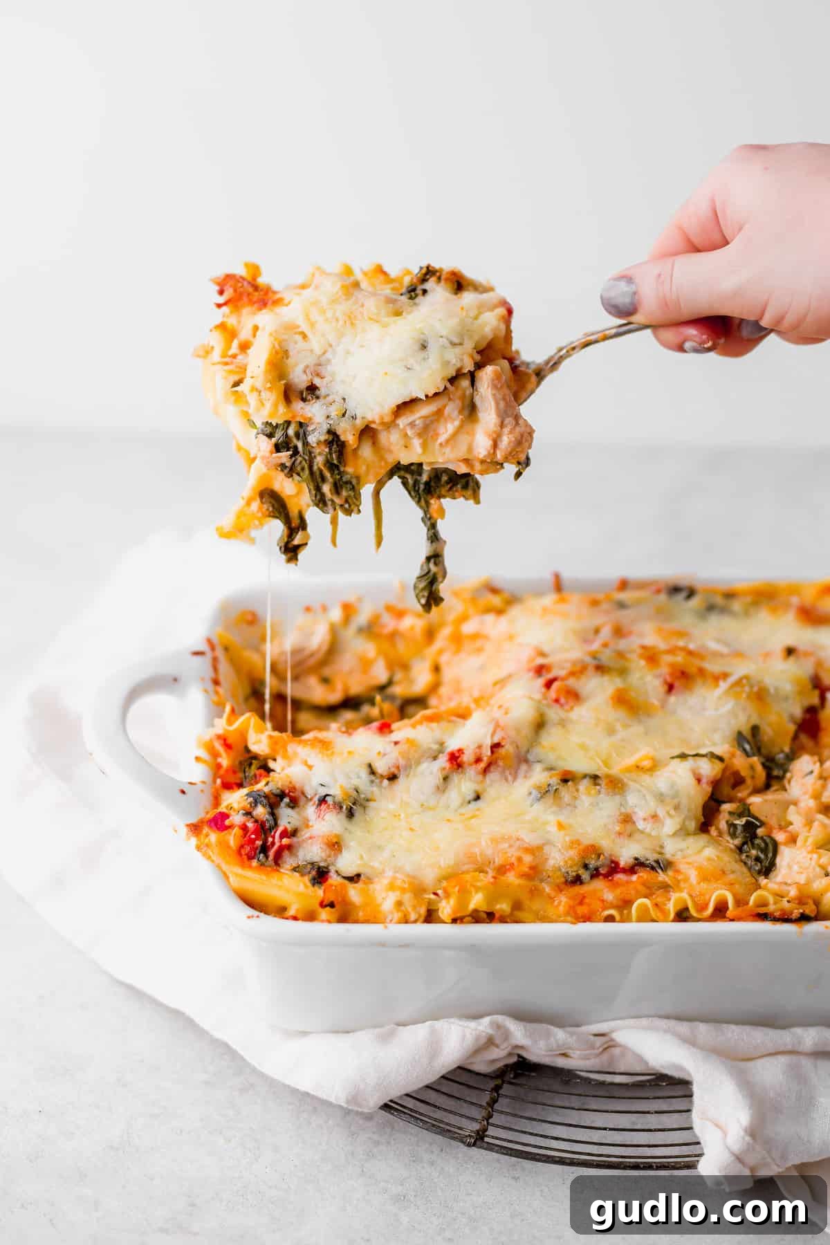 Decadent Chicken Alfredo Lasagna 7 A generous piece of Chicken Alfredo Lasagna being carefully lifted from the casserole dish with a spatula.