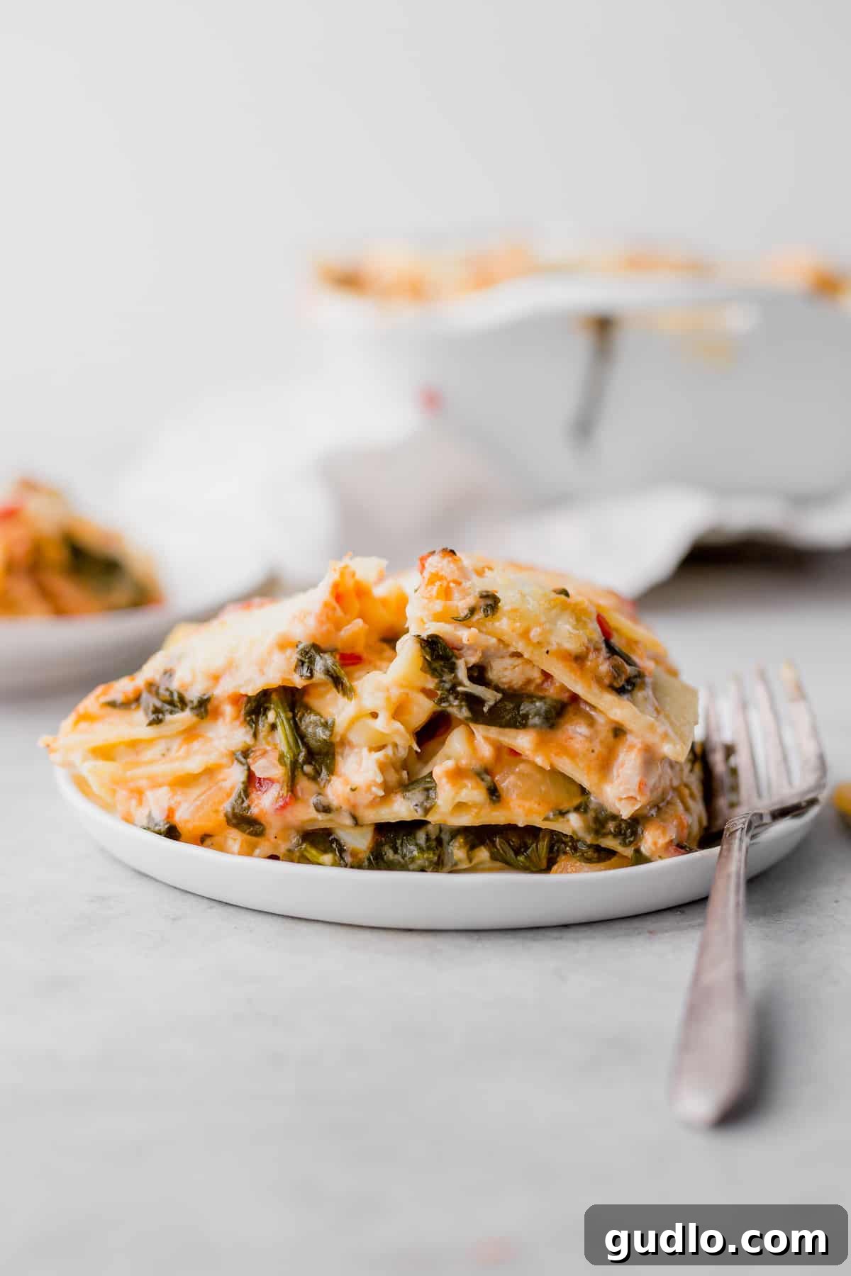 Decadent Chicken Alfredo Lasagna 9 A perfectly portioned serving of Chicken Alfredo Lasagna, adorned with fresh herbs, on a white plate.