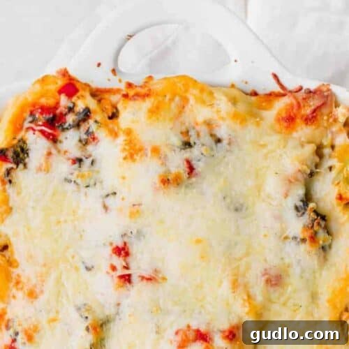 Golden Chicken Alfredo Lasagna with spinach and cheese in a white baking dish, ready to be served.