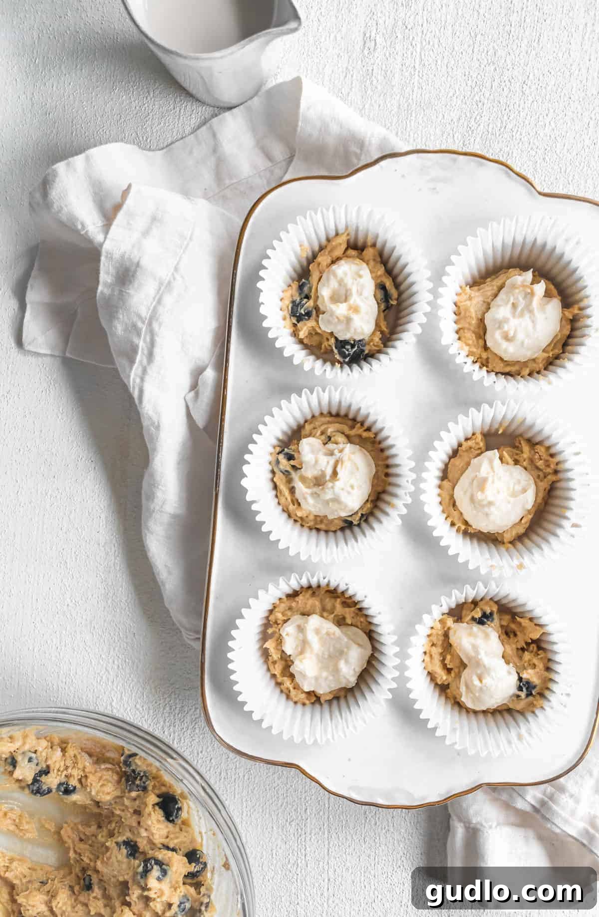 Layering Muffin Batter and Cream Cheese Filling A close-up view of muffin batter and a dollop of cream cheese filling skillfully layered into a muffin tin, awaiting baking.