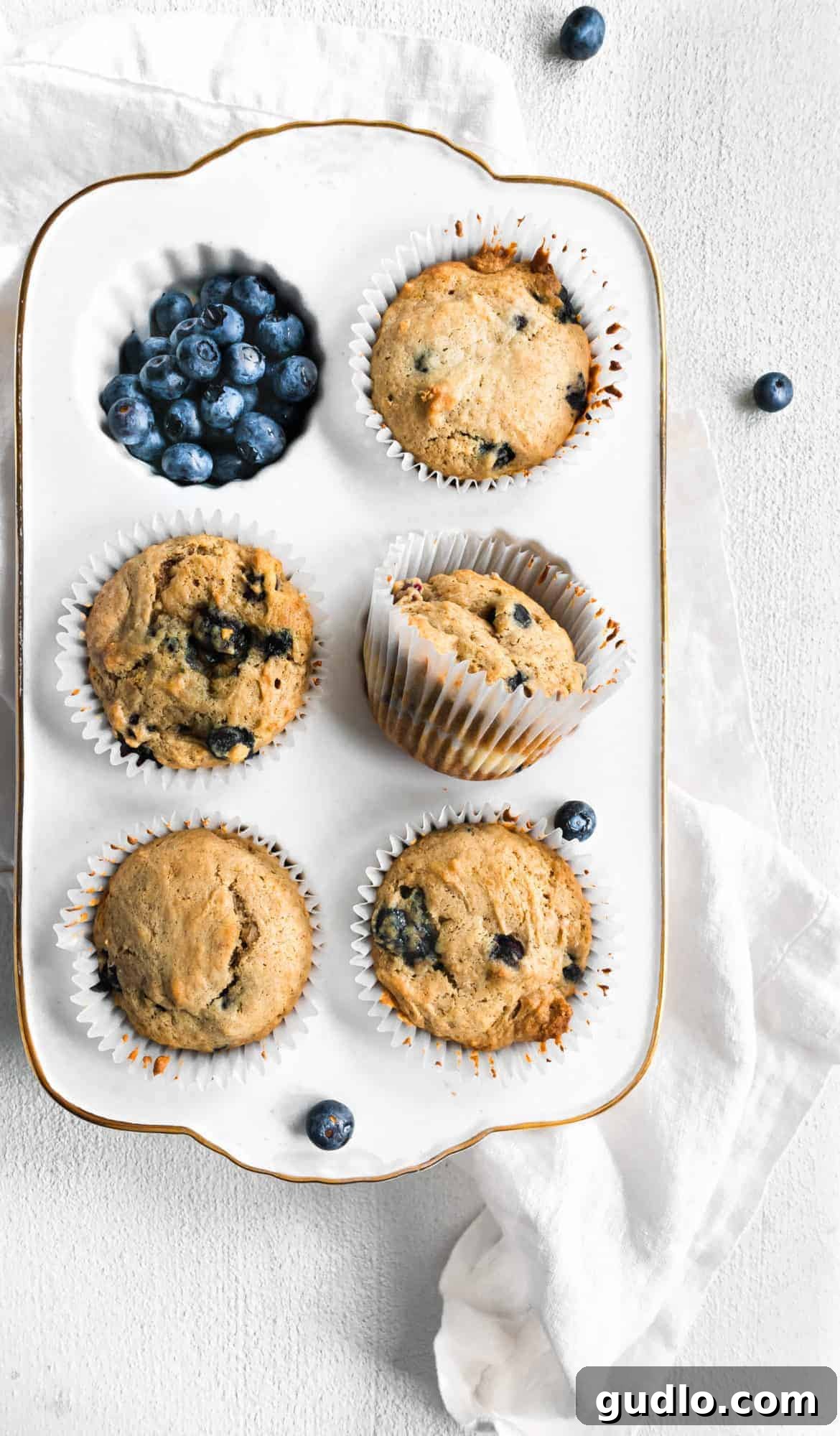 Freshly Baked Blueberry Muffins A picturesque scene of freshly baked blueberry muffins, some resting elegantly in the muffin tin, while others are presented on a rustic wooden surface alongside scattered fresh blueberries.