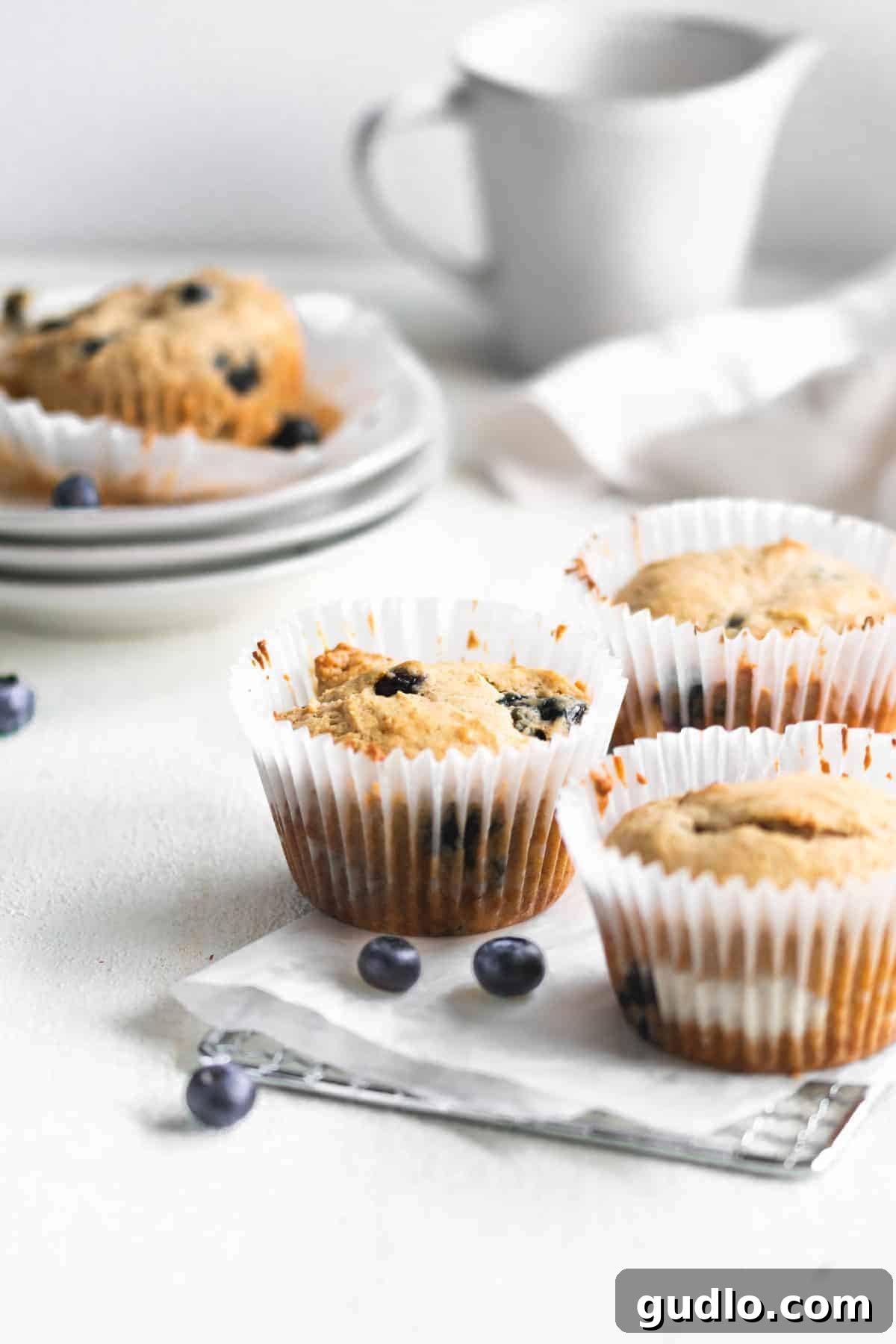 Finished Blueberry Cream Cheese Muffins Ready to Enjoy Two perfectly baked blueberry cream cheese muffins, one elegantly unwrapped and the other nestled in its paper liner, presented on a rustic wooden surface, inviting you to indulge.