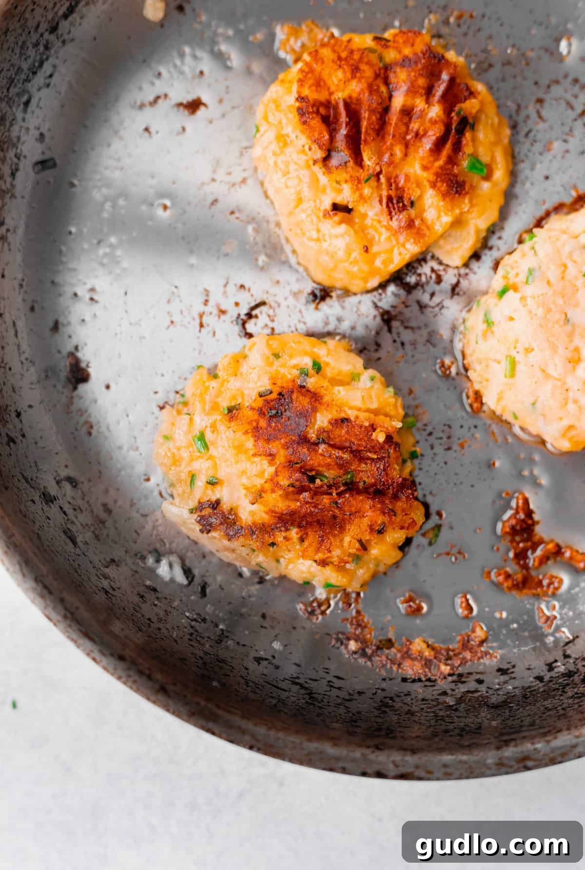 Cheesy Potato Pancakes Sizzling Three cheesy potato pancakes cooking to a golden-brown crisp in a black non-stick skillet.