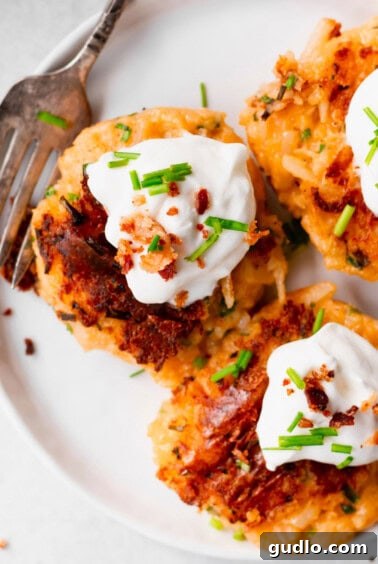 Cheesy Potato Fritters 4 A stack of golden-brown leftover cheesy potato pancakes on a plate, topped with a generous dollop of Greek yogurt and a sprinkle of fresh chives.