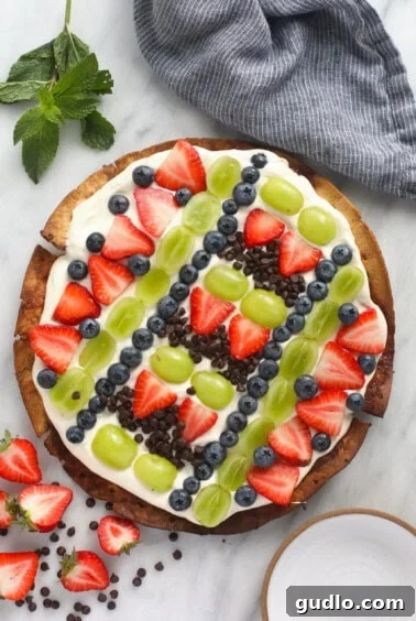 A delectable Fruit Pizza topped with juicy strawberries, fresh blueberries, and scrumptious chocolate chips, ready for serving.