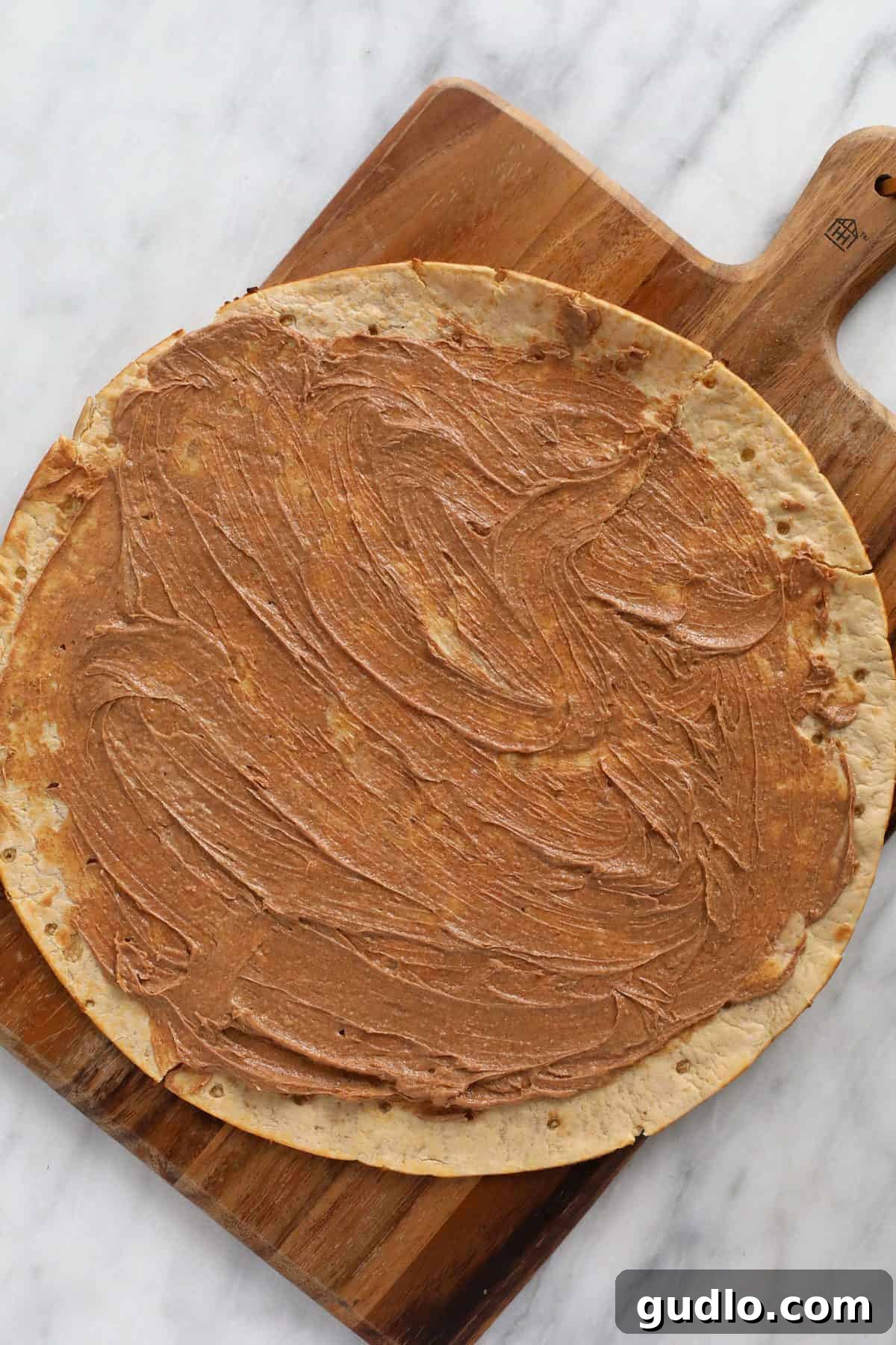 Effortless Fruit Pizza 3 A pre-made pizza crust generously slathered with cinnamon butter, ready for baking.