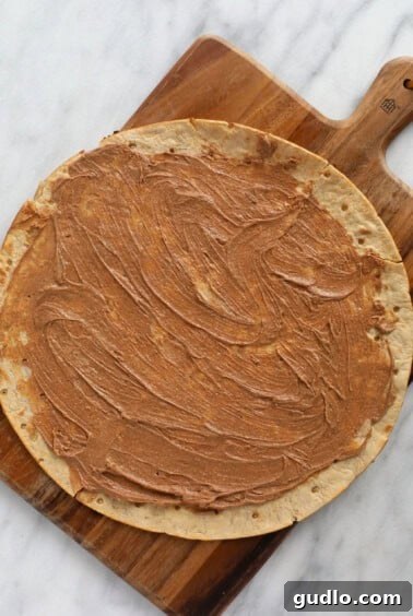 A pre-made pizza crust generously slathered with cinnamon butter, ready for baking to create a crispy fruit pizza base.