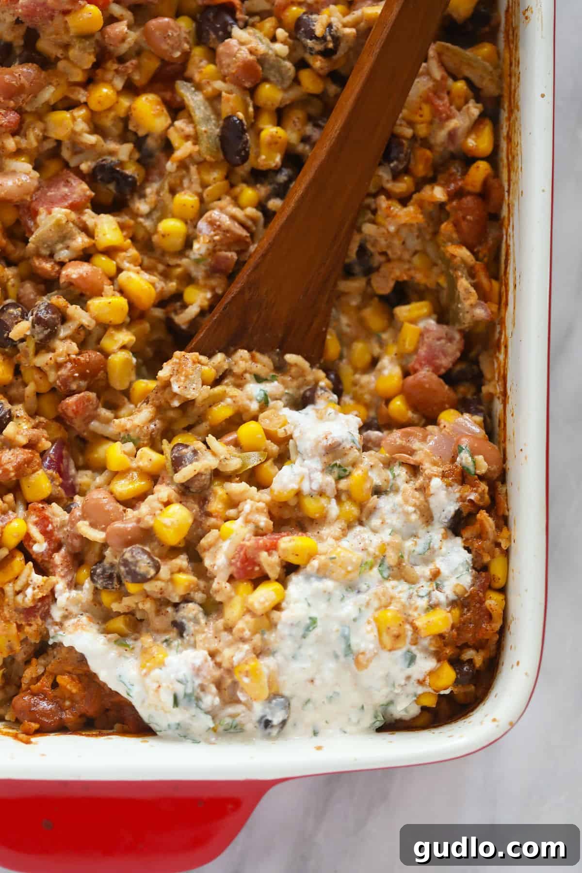 Serving up a warm, delicious portion of Mexican Street Corn Casserole. A wooden spoon scoops a hearty serving of Mexican street corn casserole from a large casserole dish, revealing its rich, layered texture.