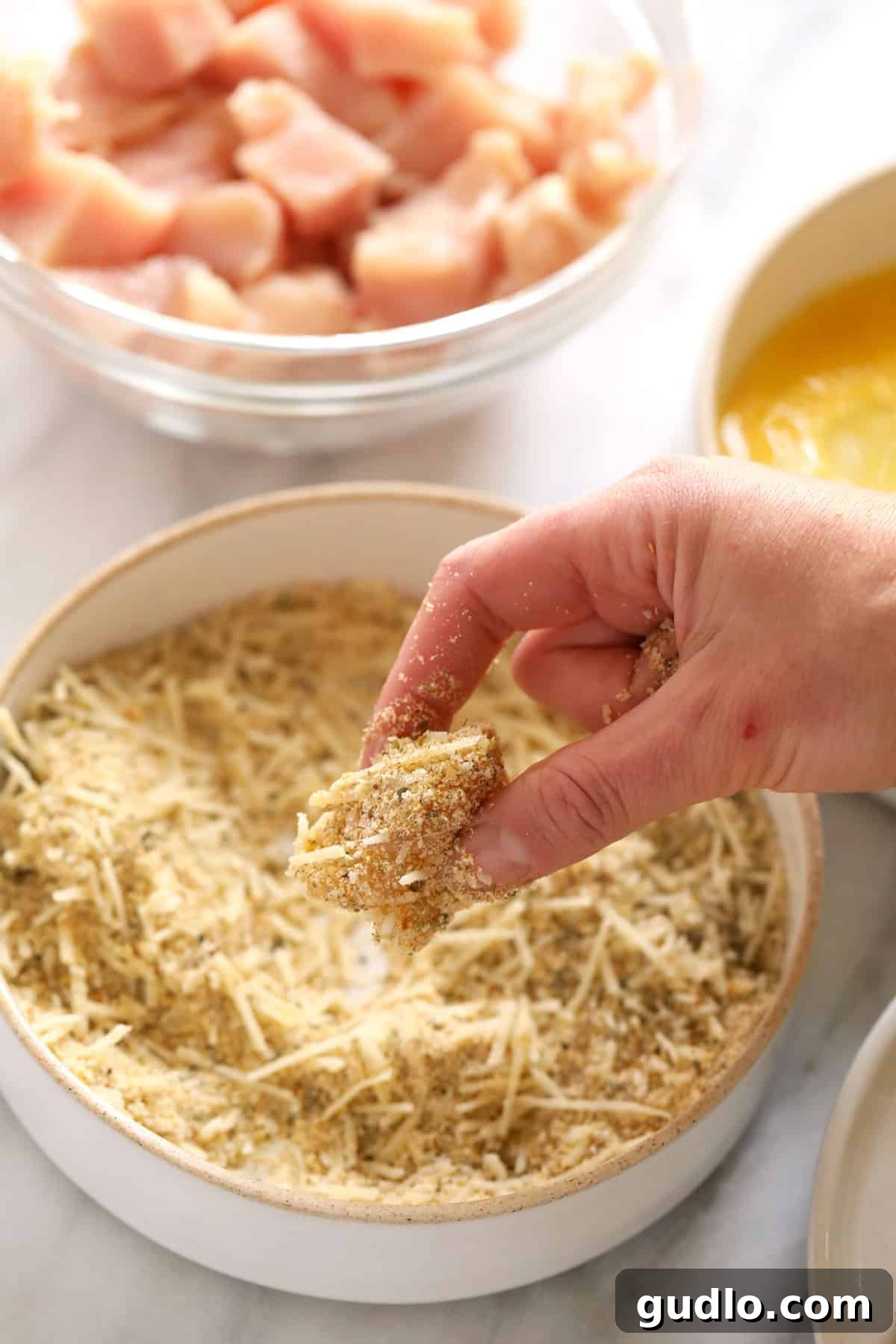 Ultimate Cheesy Chicken Parmesan Bake 3 A hand dipping a piece of chicken into bread crumbs.