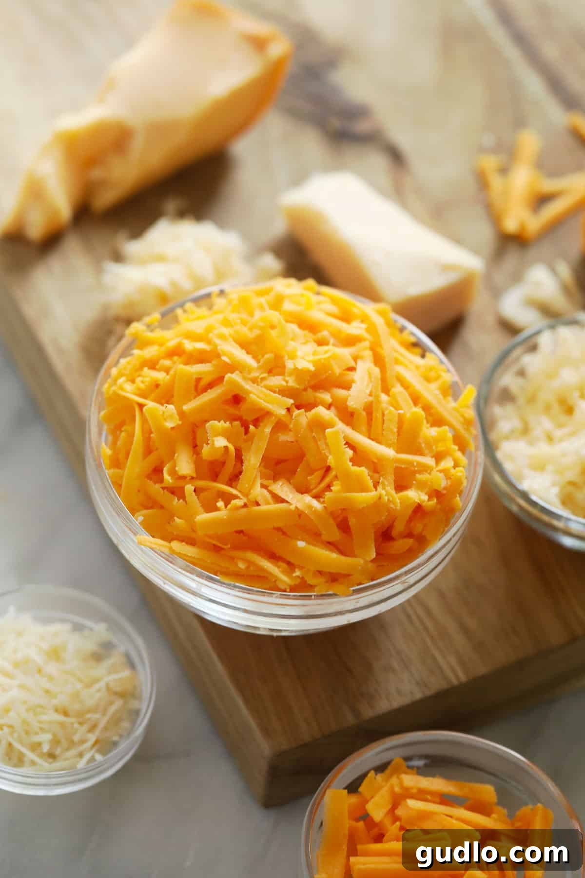 Assortment of freshly grated cheeses displayed on a wooden cutting board.