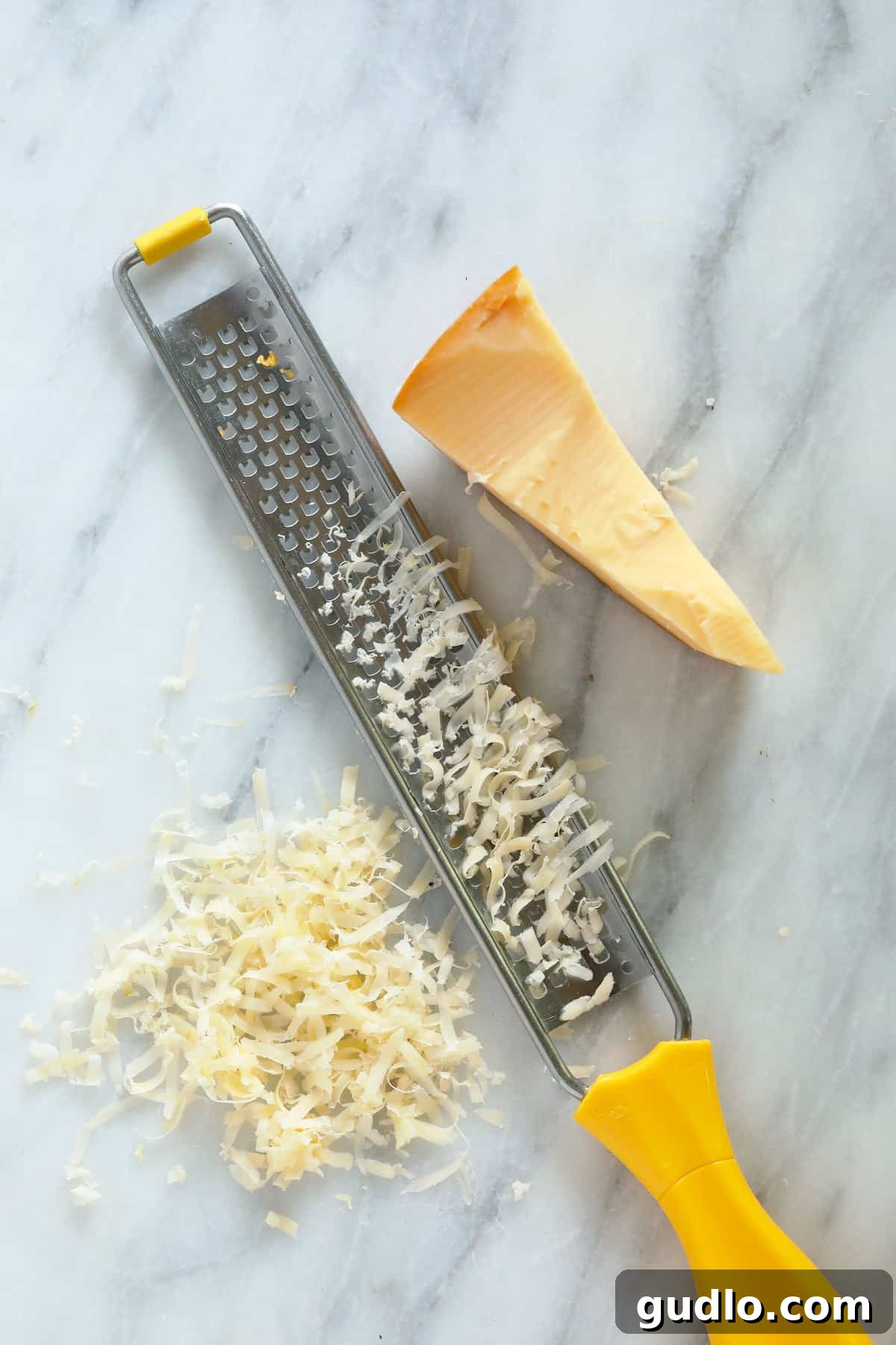 A zester next to a block of hard cheese on a wooden cutting board.