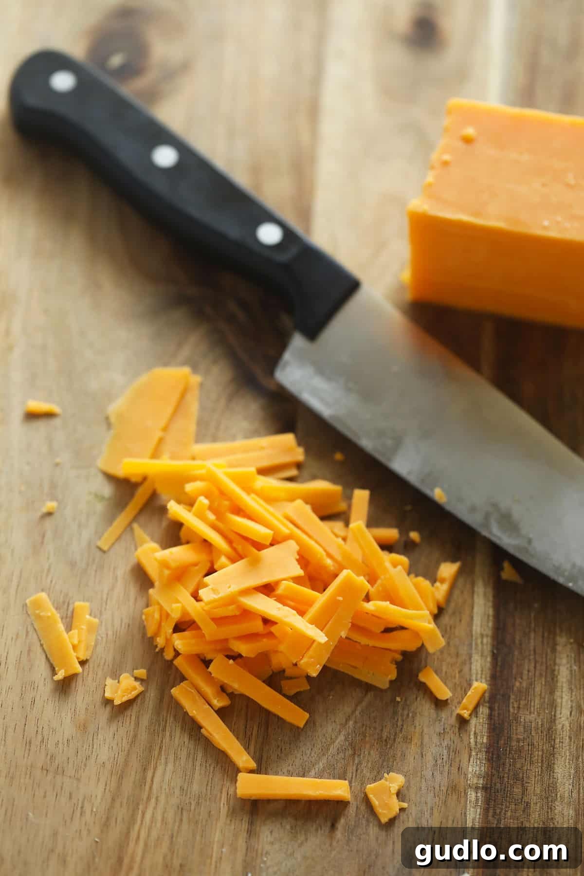 Finely shredded cheese made with a knife, lying on a cutting board next to a sharp knife.