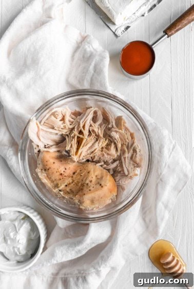 A bowl of freshly shredded chicken, generously coated in a luscious, creamy buffalo sauce, ready to be layered onto crunchy tortilla chips.